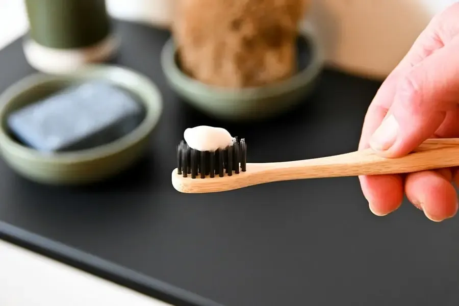 Brosse à dents en bois avec du dentifrice tenue à la main, illustrant une routine bien-être minimaliste et éco-responsable