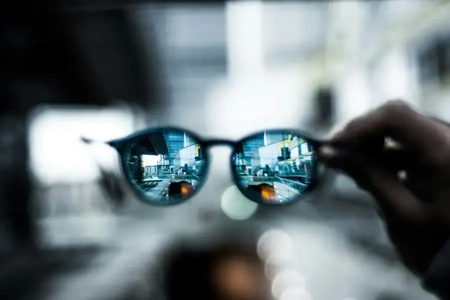 Vue urbaine nette à travers une paire de lunettes tenue à la main, illustrant la précision et la qualité de vision offerte par Regards Uniques.