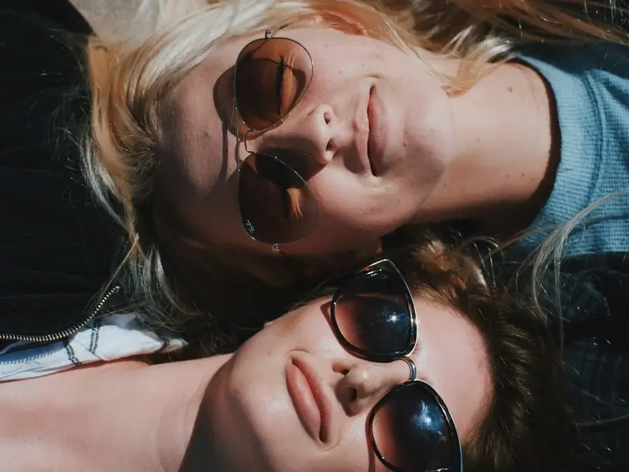 Deux femmes allongées au soleil avec des lunettes de soleil élégantes, incarnant l’esprit complice, tendance et solaire de Regards Uniques