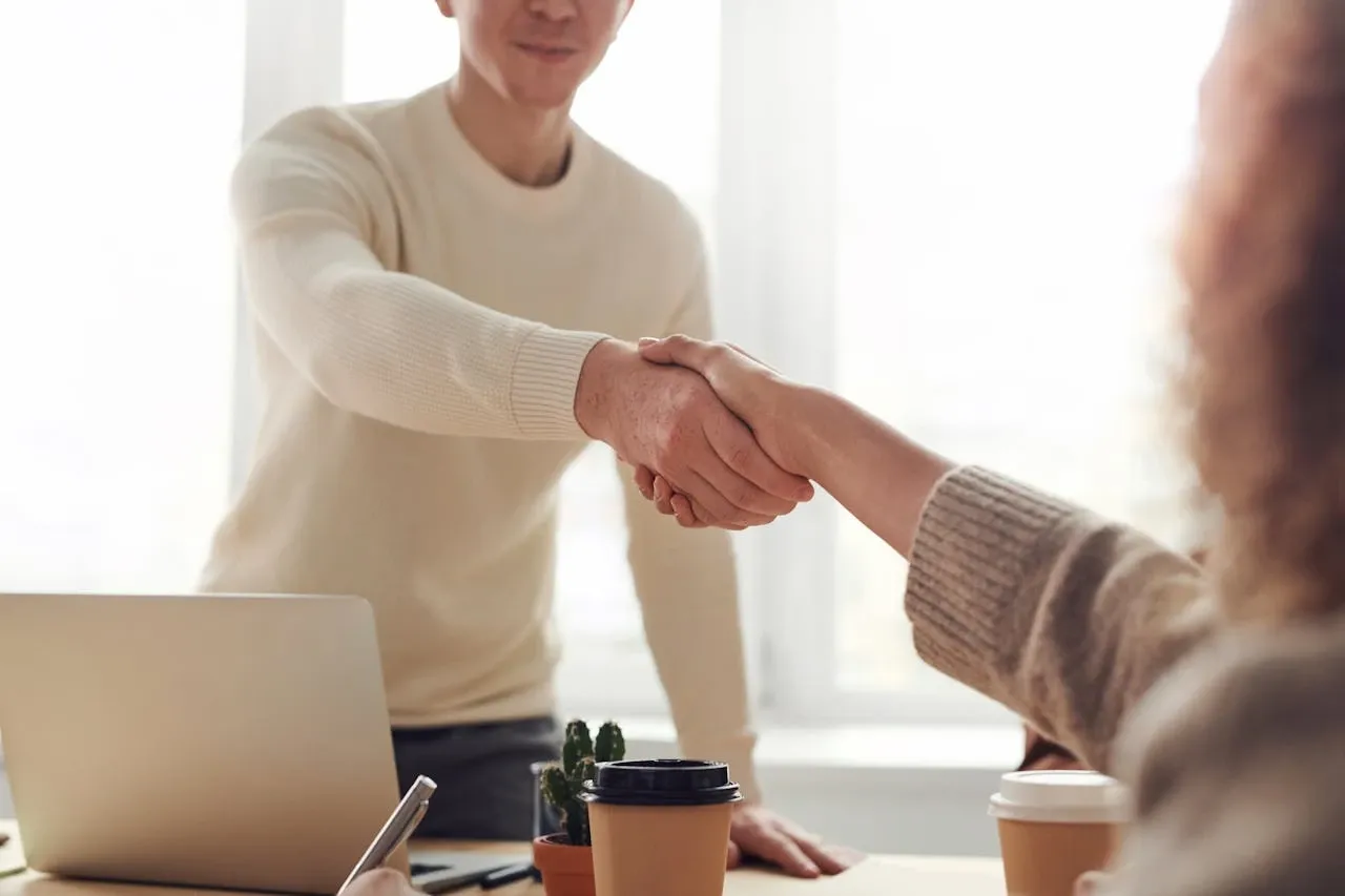Réunion d'équipe dans un environnement professionnel moderne, avec plusieurs collègues autour d'un ordinateur portable, échangeant dans une ambiance collaborative et dynamique