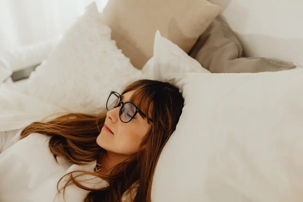 Jeune femme détendue portant des lunettes, allongée dans un lit confortable, illustrant le confort et l’élégance des montures Regards Uniques au quotidien