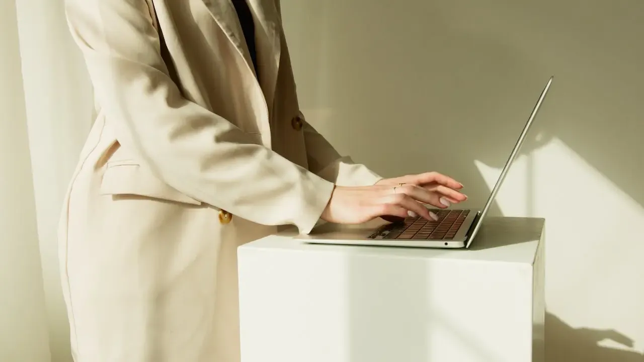 Personne élégante travaillant sur un ordinateur portable dans un espace épuré et lumineux, illustrant la modernité et le professionnalisme de Regards Uniques
